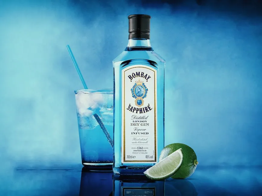 A blue glass bottle of Bombay Sapphire gin with various botanicals surrounding it on a wooden table.